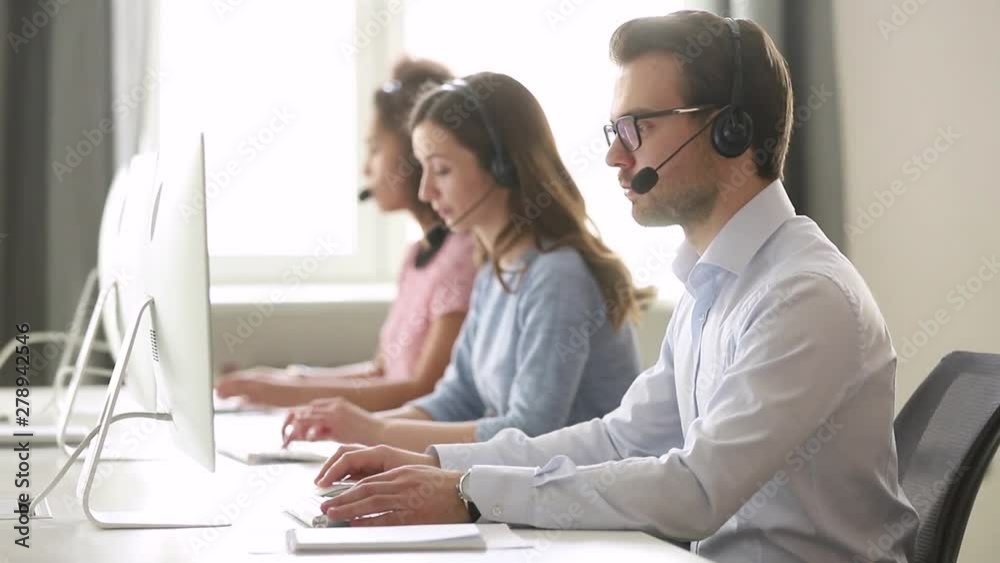 Focused male call center agent in wireless headset helping customer Focused male call center agent in wireless headset helping customer