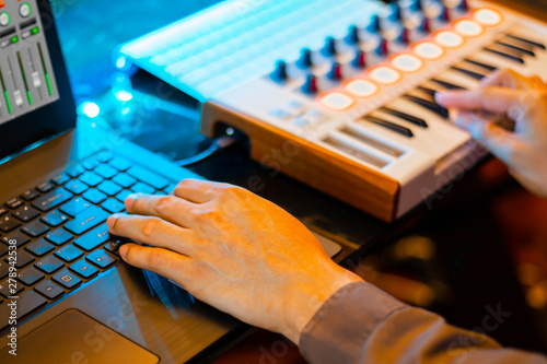 music producer hands composing a song on laptop computer and midi keyboard in home recording studio. music production concept