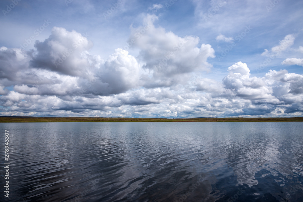 panoramic view of the blue sky with white fluffy clouds reflecting on the mirror-like surface of the water of an amazing lake