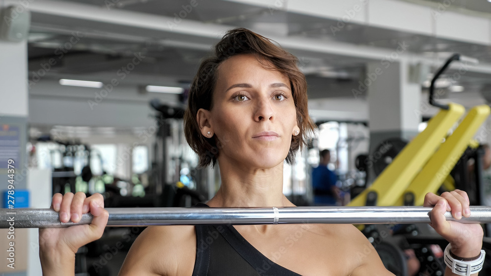 Athletic mature woman is making set of reps exercise with barbell lifting it over the head in gym. Sports workout in the gym. Athletic mature woman is making set of reps exercise with barbell lifting it over the head in gym. Sports workout in the gym.