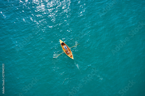 A kayak with a man moves along the birch smooth surface of water along the coastline of a resort town. Aerial photography with drone. 