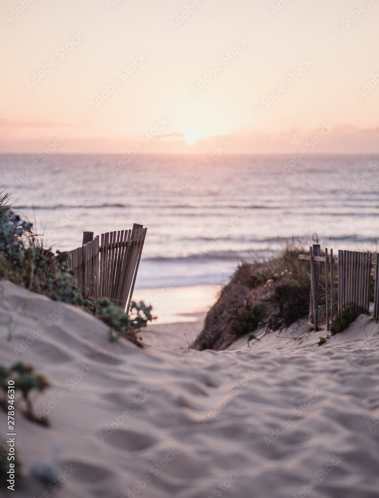 Beach path leading towards the sun setting below the sea Beach path leading towards the sun setting below the sea