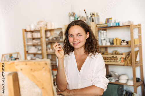 Portrait of lovely artistic woman holding piece of chalk while drawing picture in workshop