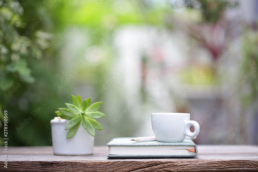 White coffee cup with small plant pot and notebook on wooden table White coffee cup with small plant pot and notebook on wooden table