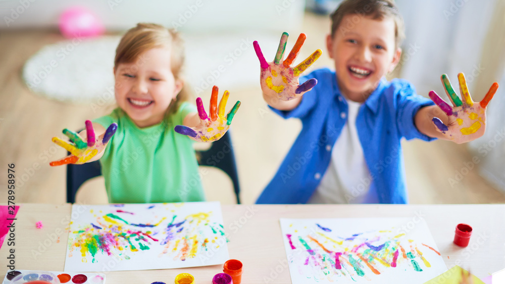 Fototapeta premium funny kids show their palms the painted paint. creative classes fine arts. two children a boy and a girl laugh. selective focusing on the palm.