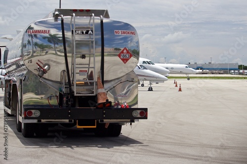 Tank truck on flight line with Jet A Fuel, no smoking, and hazmat placard on tank, air field with business jets blurred in background