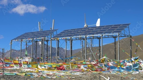 SLOW MOTION: Strong winds blow past the solar panels in the vast Tibetan plateau. Prayer flags flapping in the wind blowing across the stunning rugged landscape in the Himalayas on a sunny day.
