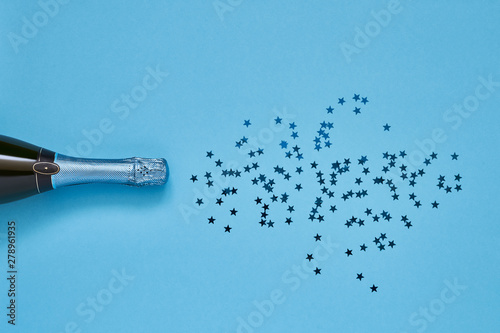 Blue Champagne bottle with blue confetti stars on light blue background. Copy space, top view.