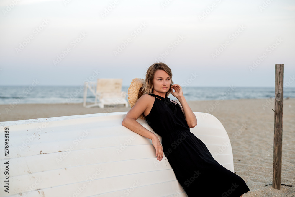 Beautiful woman in black summer dress on the beach near white wooden boat. Beautiful woman in black summer dress on the beach near white wooden boat.