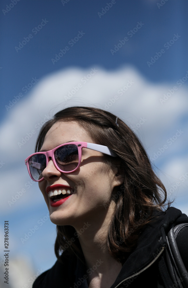 In sunglasses. Female portrait against the sky. The woman smiles a white smile. In sunglasses. Female portrait against the sky. The woman smiles a white smile.