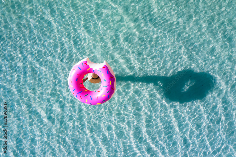 Naklejka premium top aerial view of young woman enjoy swimming on carrying on head floating inflatable tube to sea with cleared water, happy in summertime and vacation or long weekend swimming at sea .
