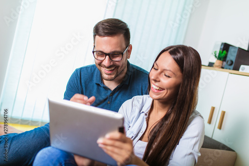 Young couple watching media content online in a tablet in the living room.