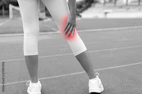 close up of Athletic woman on running track has calf cramp or Muscle injury and touching hurt leg during workout or after pulling or straining them while jogging, red highlight,black and white tone