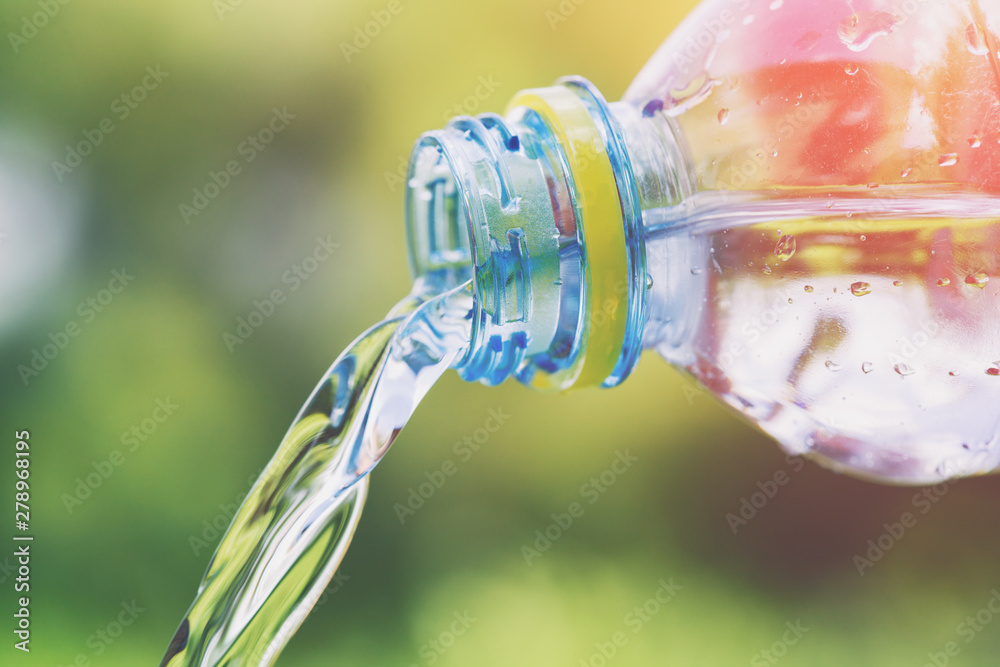 clear water pouring from plastic bottle, blurred sunny green background clear water pouring from plastic bottle, blurred sunny green background