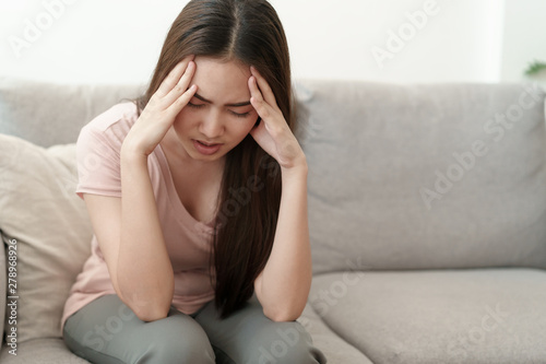 Asian woman are holding their hands to the head in pain on the sofa at home, Young women have severe headaches from migraines, Health and illness concept