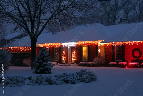 Beautiful winter blizzard evening view. Front yard of the private house covered by snow and decorated for winter holiday season glowing in the night. Christmas and New Year background.