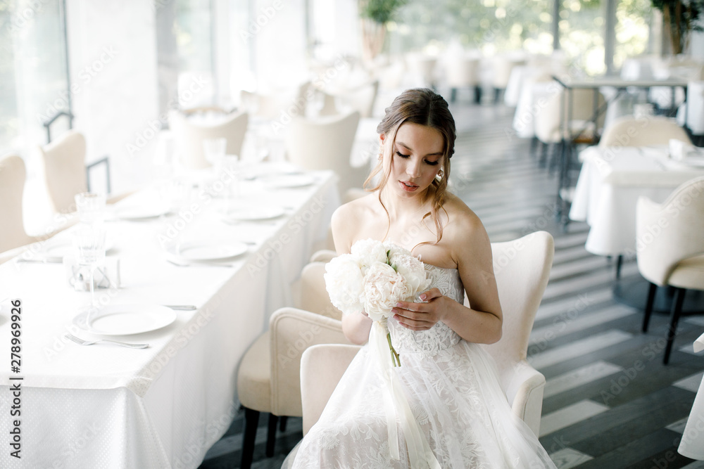 beautiful bride with a bouquet in hand, sits in a restaurant beautiful bride with a bouquet in hand, sits in a restaurant