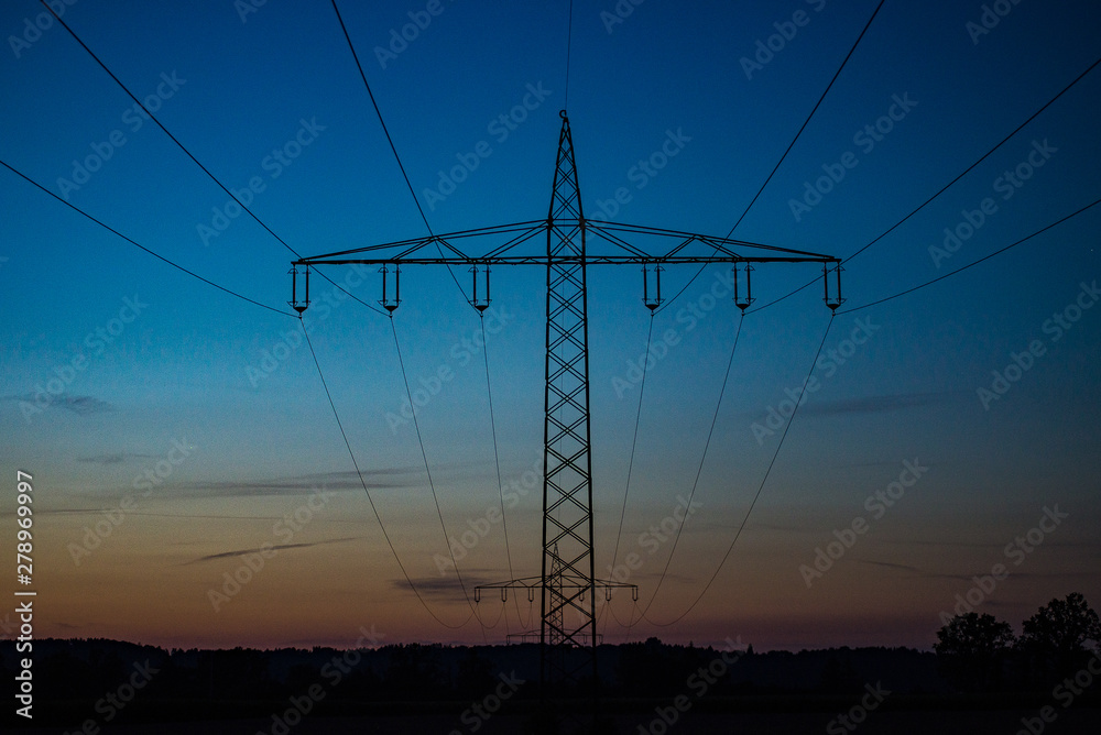 Fototapeta premium Pylons criscross the landscape against a blue sky after sunset