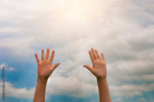 two women's hands reach for the sunlight against the blue sky with clouds