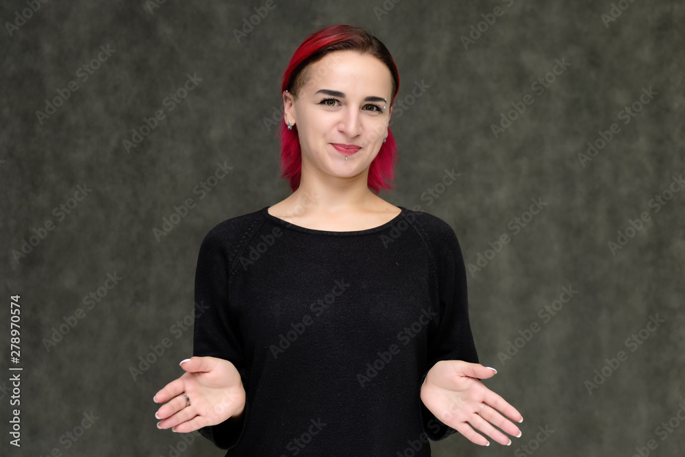 Portrait to the waist of a pretty girl with red hair on a gray background in a black jacket. Standing right in front of the camera in a studio with emotions, talking, showing hands, smiling Portrait to the waist of a pretty girl with red hair on a gray background in a black jacket. Standing right in front of the camera in a studio with emotions, talking, showing hands, smiling