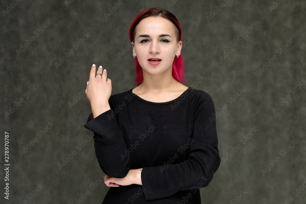 Portrait to the waist of a pretty girl with red hair on a gray background in a black jacket. Standing right in front of the camera in a studio with emotions, talking, showing hands, smiling Portrait to the waist of a pretty girl with red hair on a gray background in a black jacket. Standing right in front of the camera in a studio with emotions, talking, showing hands, smiling