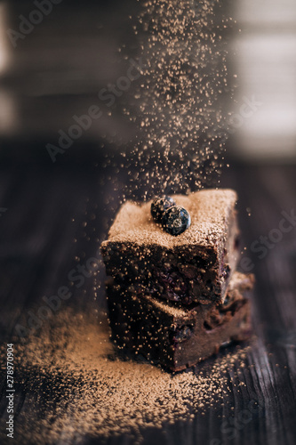 brownie cake sprinkled with ground cocoa on a dark background