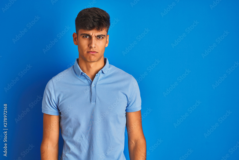 Fototapeta premium Young indian man wearing casual polo standing over isolated blue background skeptic and nervous, frowning upset because of problem. Negative person.