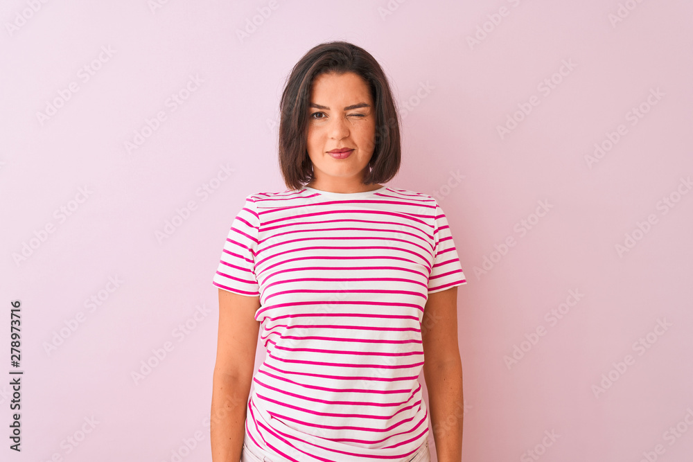 Young beautiful woman wearing striped t-shirt standing over isolated pink background winking looking at the camera with sexy expression, cheerful and happy face. Young beautiful woman wearing striped t-shirt standing over isolated pink background winking looking at the camera with sexy expression, cheerful and happy face.
