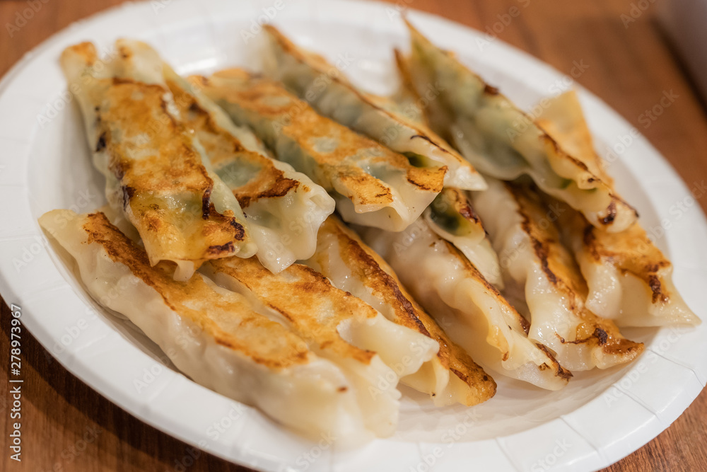 The various flavor of Pan-fried dumplings or gyoza in a paper plate placed on a wooden table.