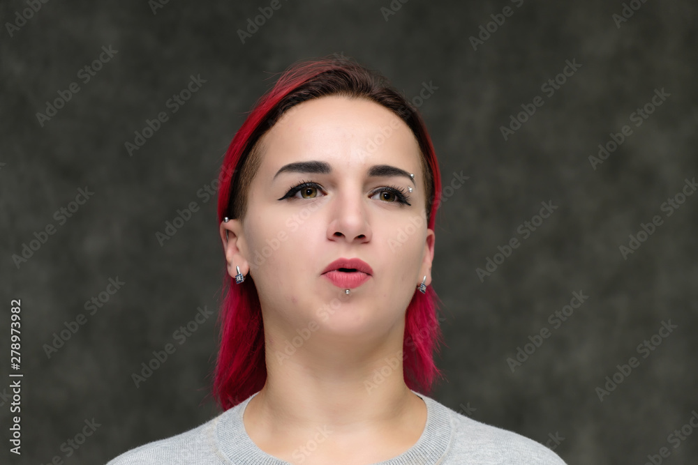 Close-up portrait on the shoulders of a pretty girl with red hair on a gray background in a gray jacket. Standing directly in front of the camera in the studio with emotions, talking, smiling. Close-up portrait on the shoulders of a pretty girl with red hair on a gray background in a gray jacket. Standing directly in front of the camera in the studio with emotions, talking, smiling.