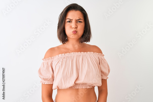 Young beautiful woman wearing casual t-shirt standing over isolated white background puffing cheeks with funny face. Mouth inflated with air, crazy expression. photo