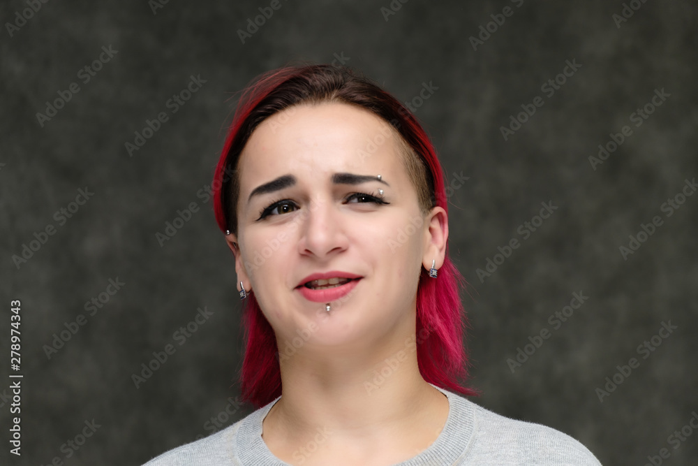 Close-up portrait on the shoulders of a pretty girl with red hair on a gray background in a gray jacket. Standing directly in front of the camera in the studio with emotions, talking, smiling. Close-up portrait on the shoulders of a pretty girl with red hair on a gray background in a gray jacket. Standing directly in front of the camera in the studio with emotions, talking, smiling.