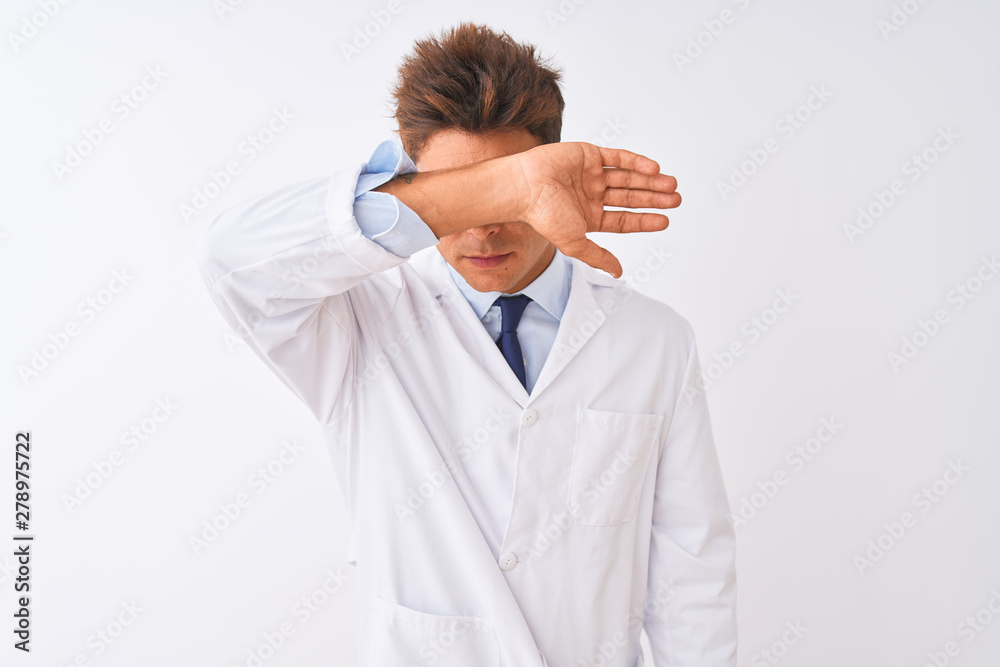 Young handsome sciencist man wearing glasses and coat over isolated white background covering eyes with arm, looking serious and sad. Sightless, hiding and rejection concept Young handsome sciencist man wearing glasses and coat over isolated white background covering eyes with arm, looking serious and sad. Sightless, hiding and rejection concept