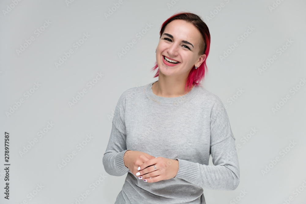 Portrait to the waist of a pretty girl with red hair on a white background in a gray sweater. Standing right in front of the camera in a studio with emotions, talking, showing hands, smiling Portrait to the waist of a pretty girl with red hair on a white background in a gray sweater. Standing right in front of the camera in a studio with emotions, talking, showing hands, smiling