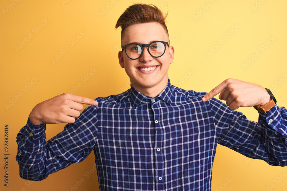 Young handsome man wearing casual shirt and glasses over isolated yellow background looking confident with smile on face, pointing oneself with fingers proud and happy. Young handsome man wearing casual shirt and glasses over isolated yellow background looking confident with smile on face, pointing oneself with fingers proud and happy.