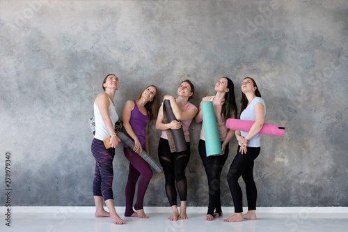 Caucasian women stand near wall with rubber mats in hands, looking up on empty copyspace. Place for your text.