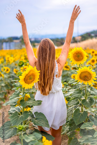 Lifestyle session. A young Caucasian blonde with short dress among sunflowers with raised arms
