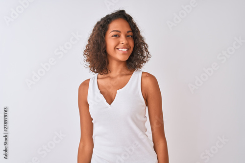Young brazilian woman wearing casual t-shirt standing over isolated white background looking away to side with smile on face, natural expression. Laughing confident.