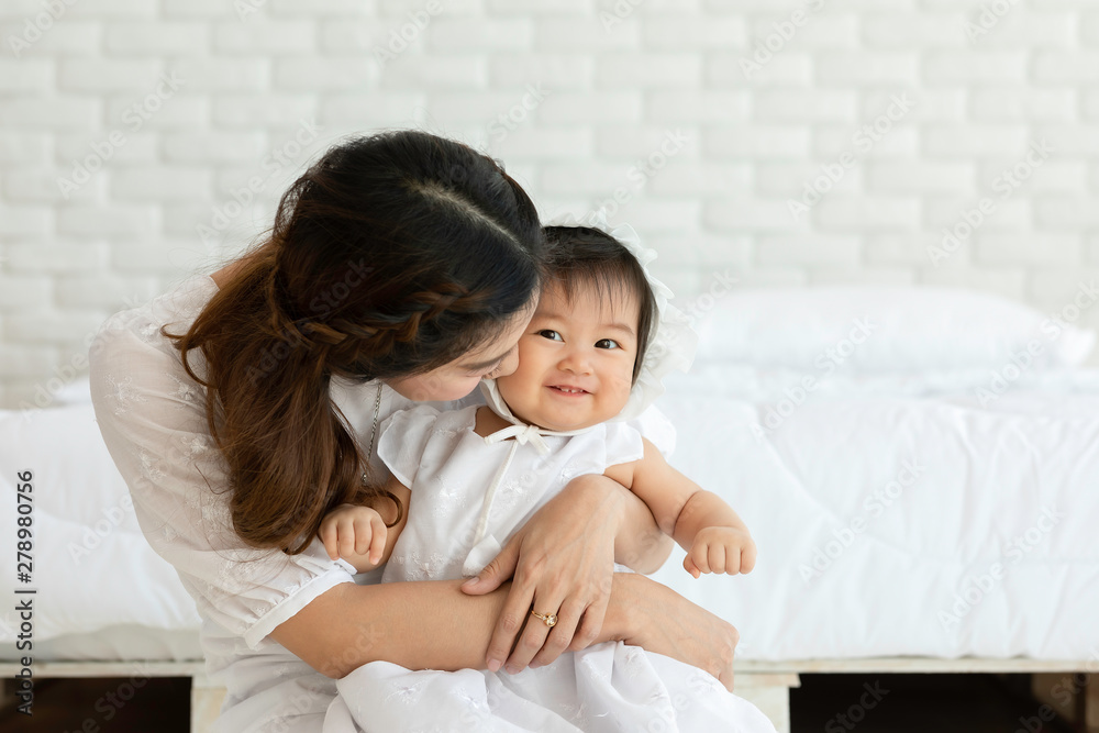 Happy Beauty mother Holding and kissing Cute Sweet Adorable Asian Baby wearing white dress sitting on Carpet smiling and playing with happiness emotional in cozy bedroom,Healthy Baby Concept Happy Beauty mother Holding and kissing Cute Sweet Adorable Asian Baby wearing white dress sitting on Carpet smiling and playing with happiness emotional in cozy bedroom,Healthy Baby Concept
