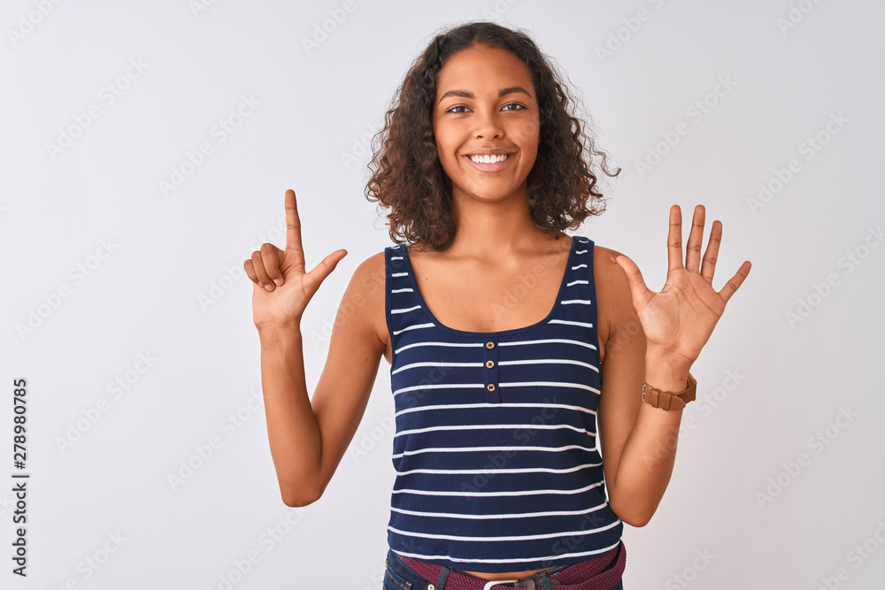 Young brazilian woman wearing striped t-shirt standing over isolated white background showing and pointing up with fingers number seven while smiling confident and happy. Young brazilian woman wearing striped t-shirt standing over isolated white background showing and pointing up with fingers number seven while smiling confident and happy.