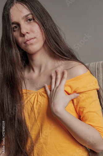 Young cute girl in yellow sweater and big glasses is combing her long hair while sitting on sofa at home. concept of hygiene and hair care