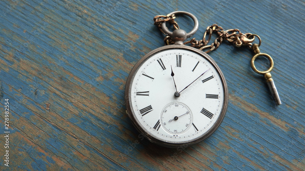 Old, silver and gold pocket watch with wind up key on weathered blue wooden background. Abstract time or nostalgia concept. Old, silver and gold pocket watch with wind up key on weathered blue wooden background. Abstract time or nostalgia concept.