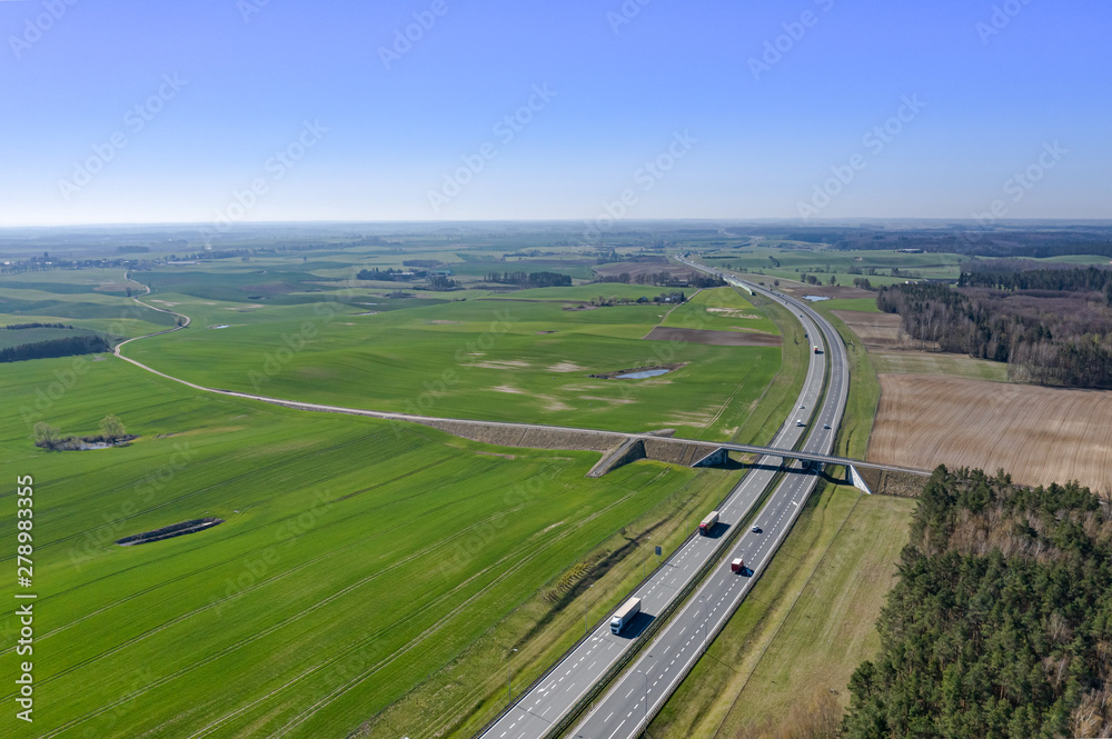 Aerial view of multi-lane highway with moving cars through countryside and forest in summer afternoon. Captured from above with a drone. Poland, A1, Europe. View of the highway with cars on top of the