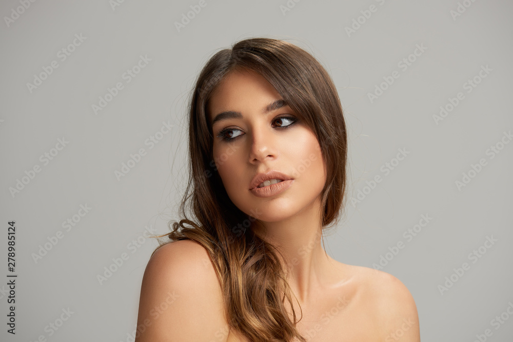 Headshot of beautiful Caucasian brunette posing in front of grey background. Beauty photography. Headshot of beautiful Caucasian brunette posing in front of grey background. Beauty photography.