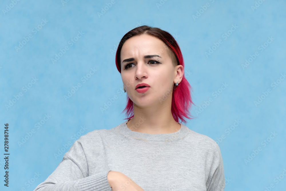 Fototapeta premium Portrait of the chest of a pretty girl with red hair on a blue background in a gray jacket. Standing in the studio right in front of the camera with emotions, talking, showing hands, smiling