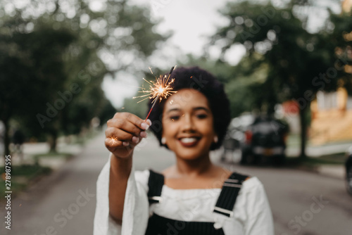 A beautiful young black woman holding up a sparkler in the summer