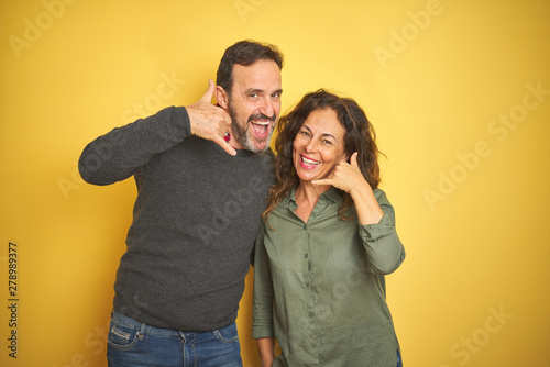 Beautiful middle age couple over isolated yellow background smiling doing phone gesture with hand and fingers like talking on the telephone. Communicating concepts.