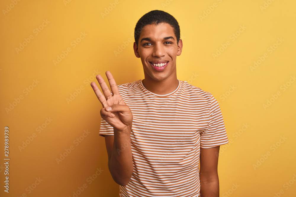 Young handsome arab man wearing striped t-shirt standing over isolated yellow background showing and pointing up with fingers number three while smiling confident and happy. Young handsome arab man wearing striped t-shirt standing over isolated yellow background showing and pointing up with fingers number three while smiling confident and happy.