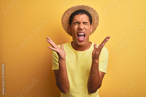 Young handsome arab man wearing t-shirt and summer hat over isolated yelllow background celebrating mad and crazy for success with arms raised and closed eyes screaming excited. Winner concept