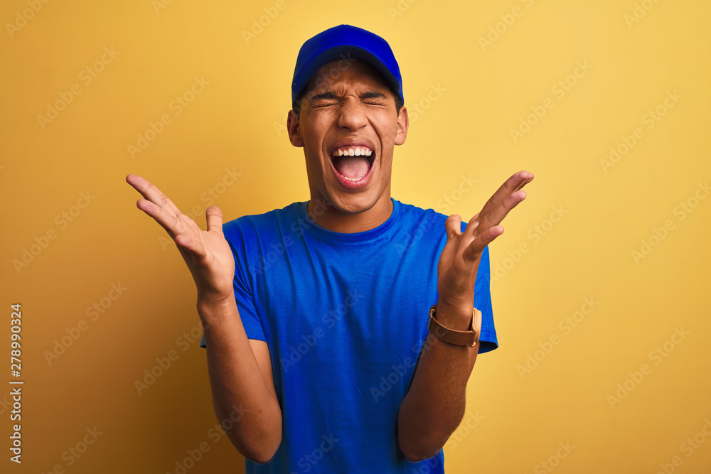 Young handsome arab delivery man standing over isolated yellow background celebrating mad and crazy for success with arms raised and closed eyes screaming excited. Winner concept